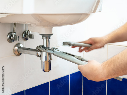 plumber adjusts pipe-wrenches to install a siphon photo