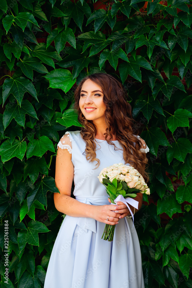 cute smile of girl in a beautiful dress that holds a bunch of flowers in the background of green leaves cute smile of girl in a beautiful dress that holds a bunch of flowers in the background of green leaves