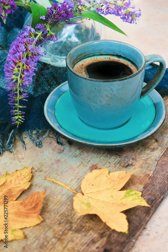 View of a blue vintage cup of black coffee, purple flowers and golden yellow leaves on a blue checkered scarf. Good morning or hello autumn background