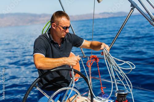 Man skipper at the helm controls of a sailing yacht.
