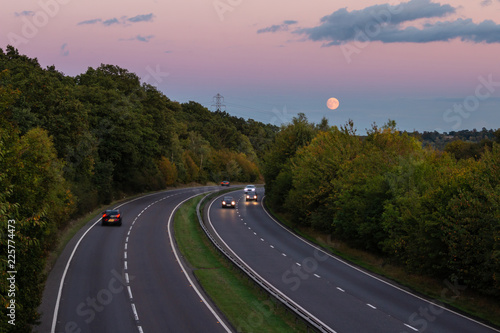 British dual carriageway road during sunset with rising full moon in the background