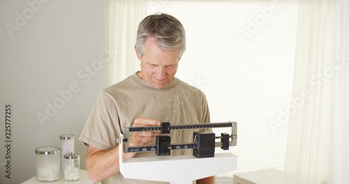 Obraz na plátně Healthy mid-aged caucasian man weighing himself on scale