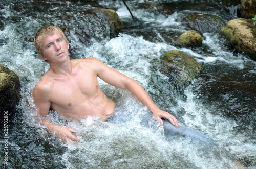 handsome man resting on the river lying in a waterfall among the stones