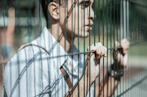 Always believe. Selective focus of tender male hands touching fence and guy thinking