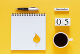 Autumn composition. Wooden calendar November 5 cup of coffee, empty open notepad with pen and yellow oak leaf on yellow background. Top view Flat lay Mockup Concept Hello November