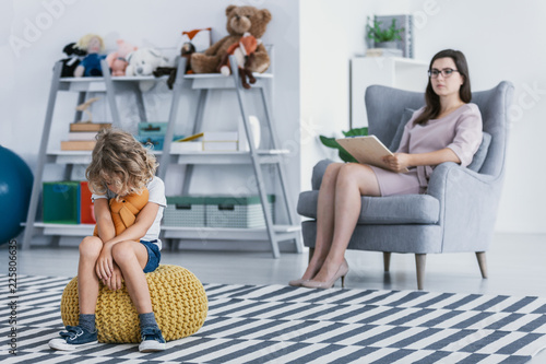 Εκτύπωση καμβά A withdrawn child with an autism spectrum disorder sitting on a pouf during an evaluation session with a professional therapist in an office
