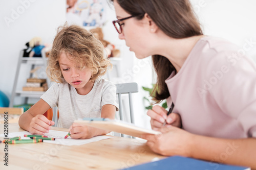 A psychotherapist watching a child draw pictures with crayons during an evaluation in a private school.