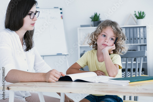 An absent-minded kid looking to the side and not at his homework notebook during a lesson with a tutor.