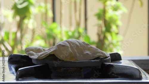 footage of making of Phulka a kind of Chapati: Indian thin bread made from wheat dough being baked on gas stove in home.