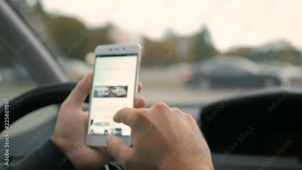 Man chooses to buy a car on the site. Looking at used vehicle to buy on a smartphone app. Driver reads news on mobile phone inside car. Screen is blurred. Focus on finger hand. Man chooses to buy a car on the site. Looking at used vehicle to buy on a smartphone app. Driver reads news on mobile phone inside car. Screen is blurred. Focus on finger hand.