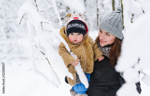 Mother and baby son embracing in a winter park amoung trees branches.