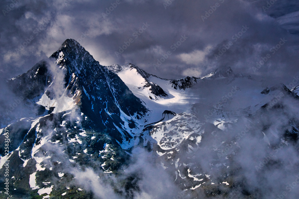 ośnieżone szczyty alpejskie w chmurach i mgłach - obrazy, fototapety, plakaty 
