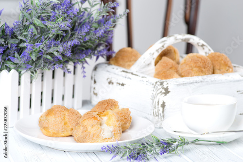 Many tasty cakes of Shue from custard paste with cream stuffing lie on a round plate on a white wooden table. photo