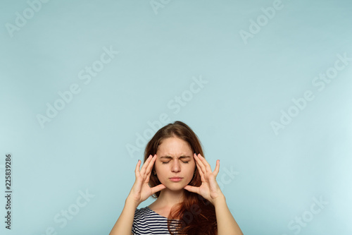headache and migraine. fatigue and exhaustion. woman massaging temples with hands. pain meds or stress relieving techniques concept. young girl portrait on blue background. photo