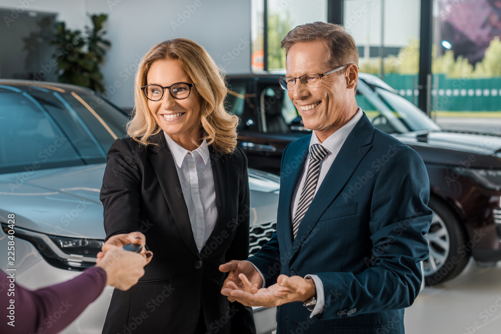 partial view of female car dealer giving car key to smiling couple in formal wear in dealership salon partial view of female car dealer giving car key to smiling couple in formal wear in dealership salon