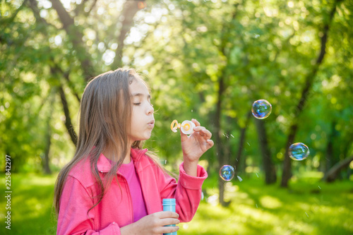 A little girl blowing soap bubbles in summer park