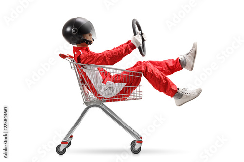 Guy in a racing suit with helmet holding a steering wheel and sitting inside a shopping cart © Ljupco Smokovski