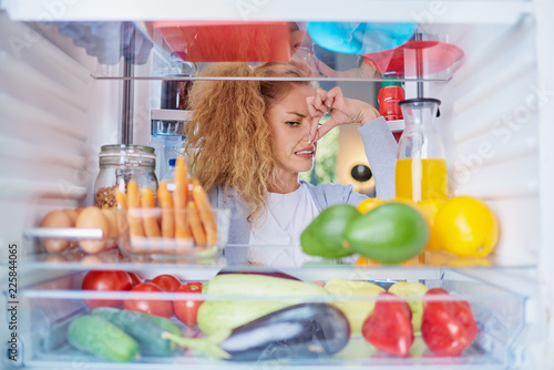 Fotografie Womann standing in front of opened fridge and holding up to her nose because of bad smell
