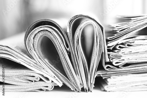 Lots of newspapers folded and stacked in pile and heart made of pages with news. Concept for reading. Stack of papers and magazines, side view, selective focus             