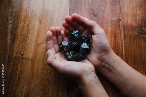 Girl with cupped hands at table holding role playing dice, close up photo