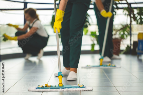 Close-up on cleaning specialist with yellow gloves holding mop while wiping floor