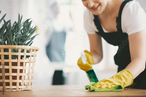 Close-up on housewife with yellow gloves and cloth cleaning a table at home