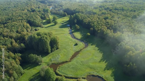 Aerial view of beautiful curvy river flowing between forest and green grassland