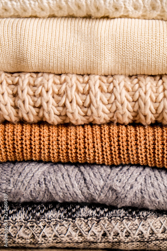 Fototapeta Naklejka Na Ścianę i Meble -  Bunch of knitted warm pastel color sweaters with different knitting patterns folded in stack, clearly visible texture. Stylish fall / winter season knitwear clothing. Close up, copy space for text.
