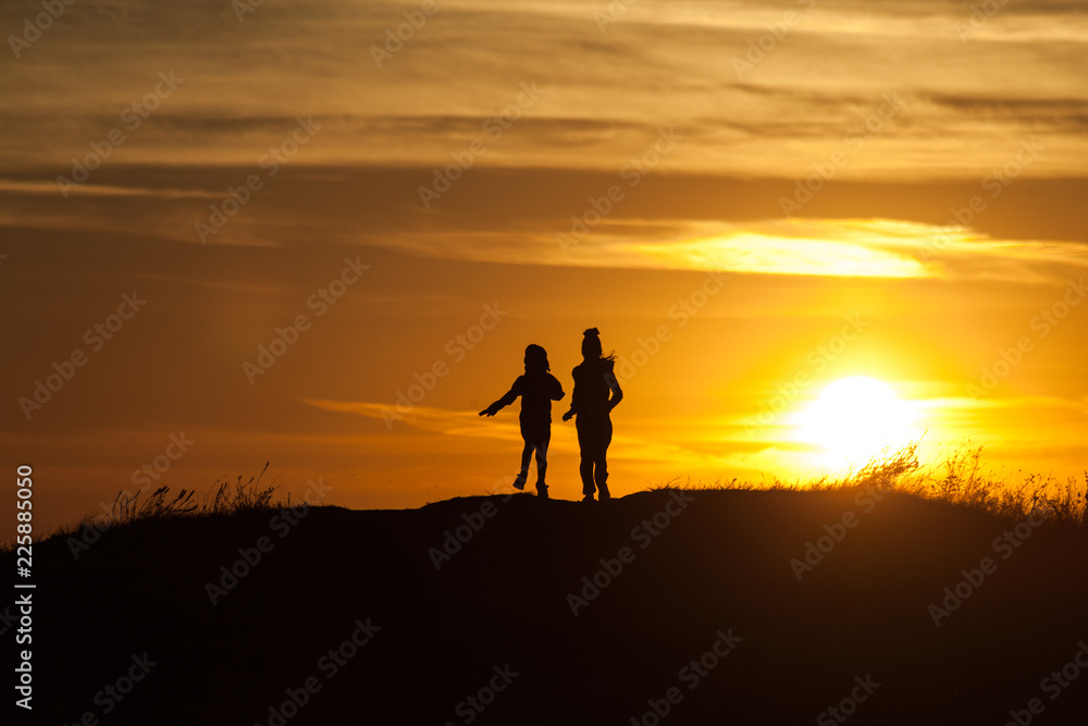 Two silhouettes of a child at sunset background