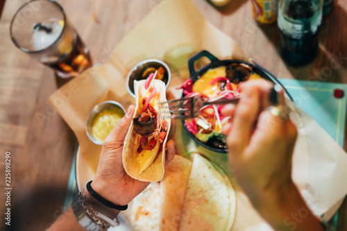 Young woman preparing and eating mexican food in a street restaurant.  Mexican tacos, nachos and wings. Top view.