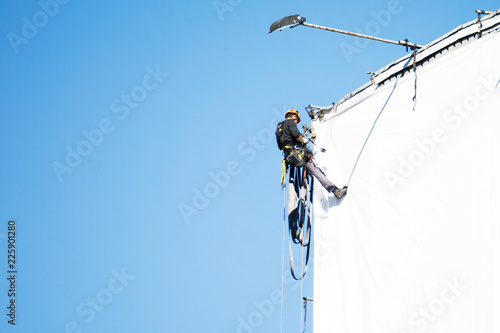 An industrial climber hangs an advertising banner on a commercial building extreme, against the blue sky photo