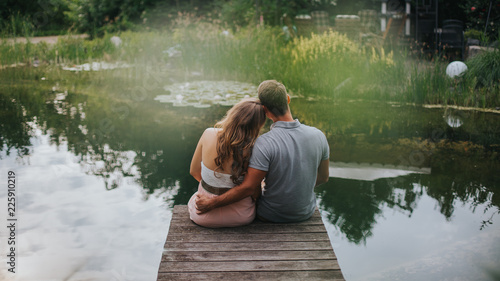 Rückansicht von glücklichem Paar, dass auf einem Stag am See sitzt