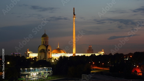 Moscow / Russia - Evening view to the Park Pobedy at poklonnaya hill - Victory park, church, stele and monument museum in summer against silhouette trees and dark blue sky with clouds