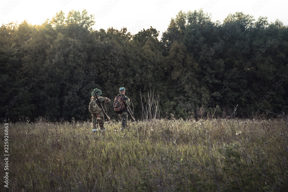 Hunting hunters in rural field nearby forest at sunset during hunting season Hunting hunters in rural field nearby forest at sunset during hunting season