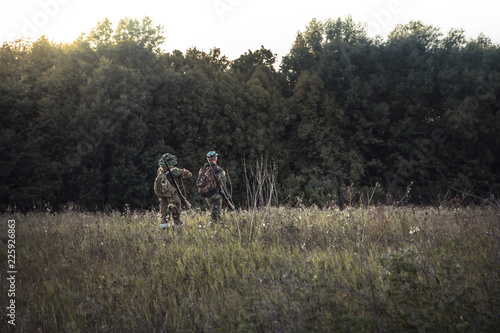 Hunting hunters in rural field nearby forest at sunset during hunting season