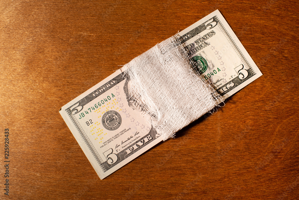 Five-dollar bills bandaged with a bandage on a wooden background. Five-dollar bills bandaged with a bandage on a wooden background.