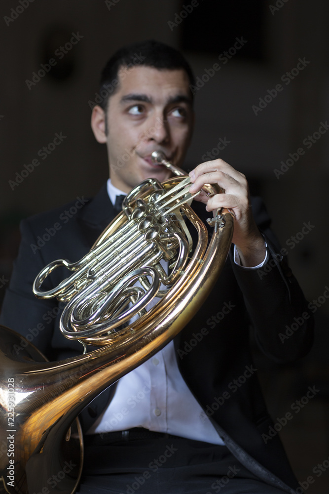 Fototapeta premium French horn player. Hornist playing brass orchestra music instrument.