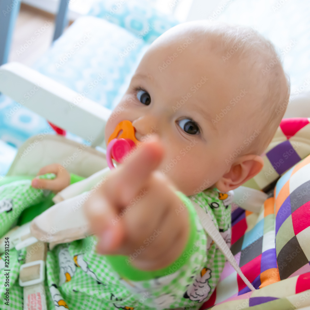 One year old baby nibbles / sucks on a rubber nipple because his teeth are being cut. Little cheerful boy in a light green suit with sheep. Soft focus, bokeh One year old baby nibbles / sucks on a rubber nipple because his teeth are being cut. Little cheerful boy in a light green suit with sheep. Soft focus, bokeh
