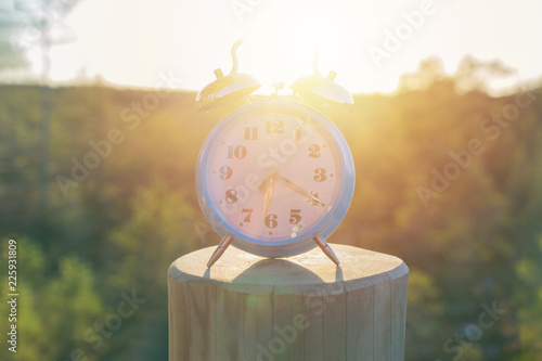 Vintage blue alarm clock on summer forest background. Daylight saving time concept winter or summer Europe time, toned