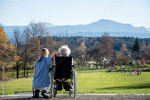 Seniorin im Rollstuhl blickt mit ihrer Pflegerin in die Allgäuer Berge