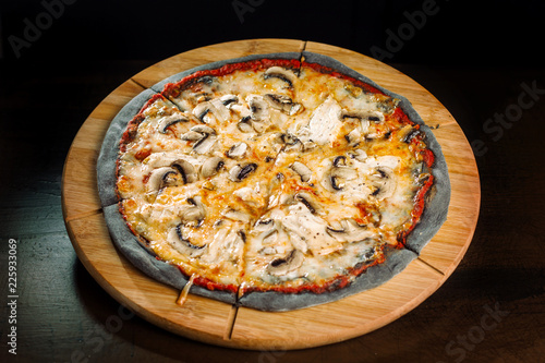 Pizza with champignons and chicken breast on black dough.