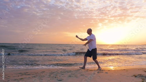 Man training Taijiquan during morning sunrise in sky on sea beach photo