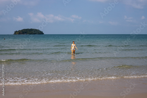 Girl walking out of sea water on white sand beach. Tropical seashore view with lonely tourist. Sole traveler