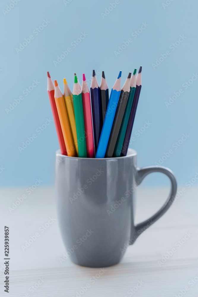 Gray mug with colored pencils on a blue background, blur. Gray mug with colored pencils on a blue background, blur.