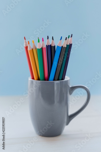 Gray mug with colored pencils on a blue background, blur.