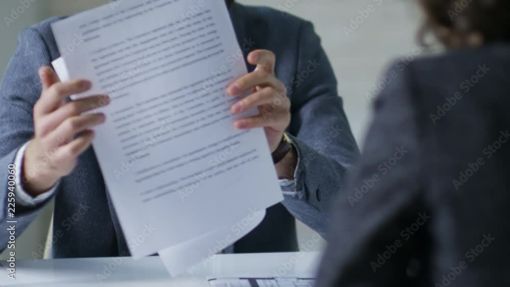 Young bearded businessman giving two paged document with terms and conditions printed on it to unrecognizable female client seen from her back Young bearded businessman giving two paged document with terms and conditions printed on it to unrecognizable female client seen from her back
