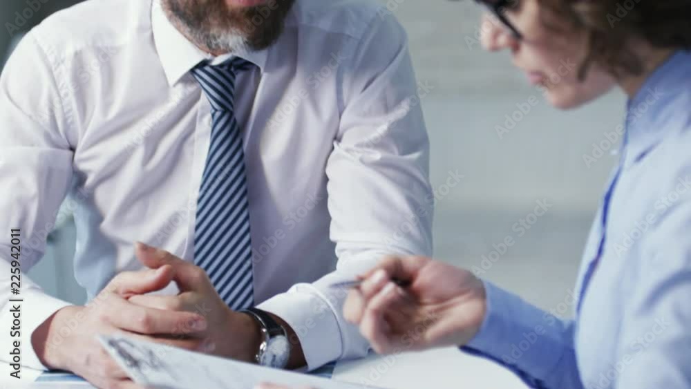 Tilt down shot of two business partners, man and woman, sitting at office desk, woman filling out contract of agreement Tilt down shot of two business partners, man and woman, sitting at office desk, woman filling out contract of agreement