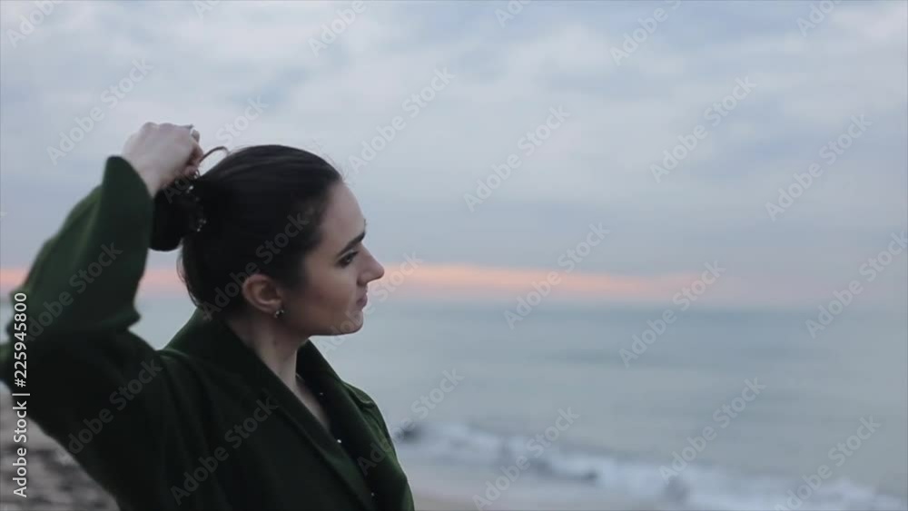 Beautiful sunrise sky over the sea. Side half-body view of a beautiful girl undoing her long dark hair and enjoying the view. Focus shifting from the girl to the nature Beautiful sunrise sky over the sea. Side half-body view of a beautiful girl undoing her long dark hair and enjoying the view. Focus shifting from the girl to the nature