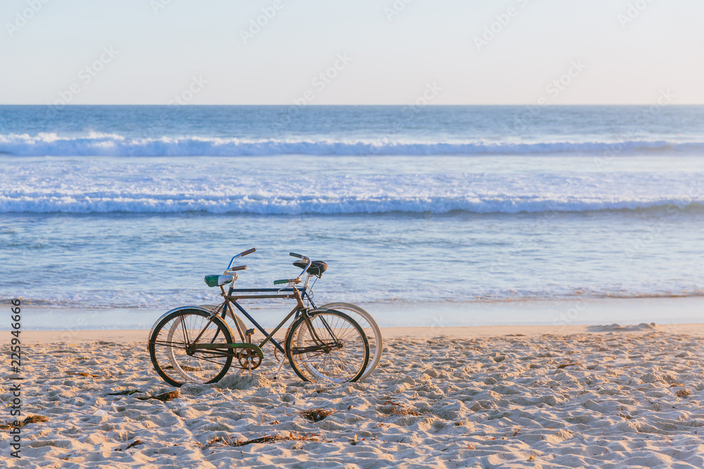 Fototapeta premium Two bikes on beach against ocean waves