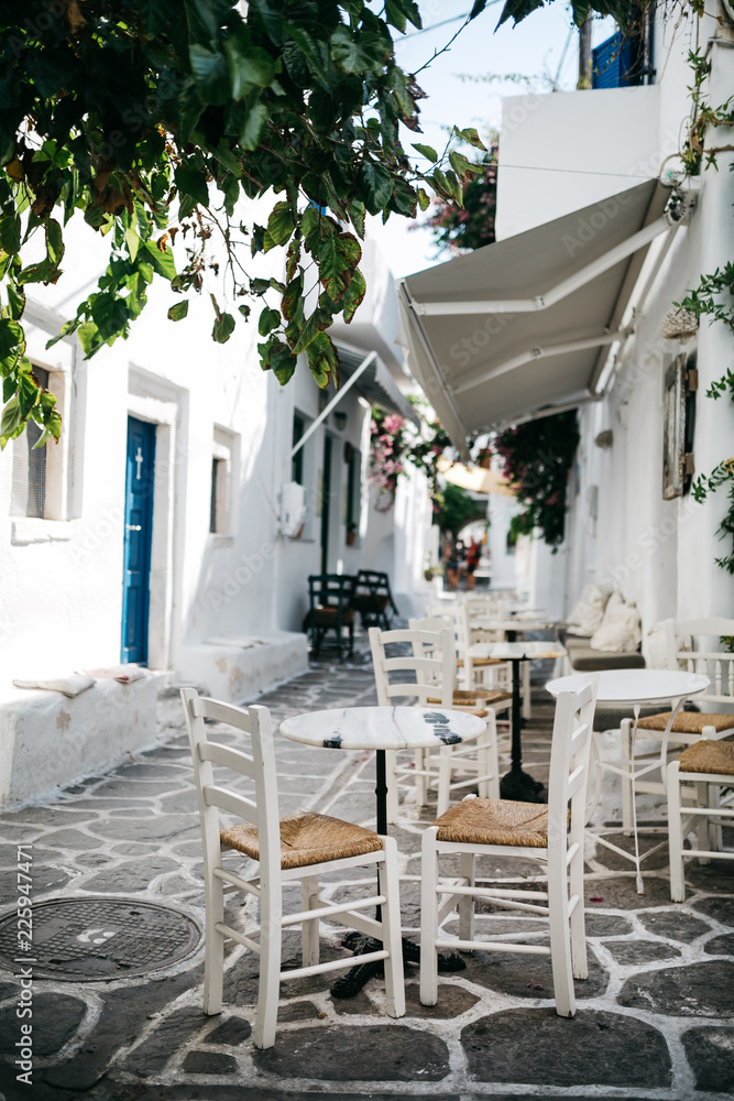 Fototapeta premium White table and chairs on a white street of Naussa, Paros island, Greece